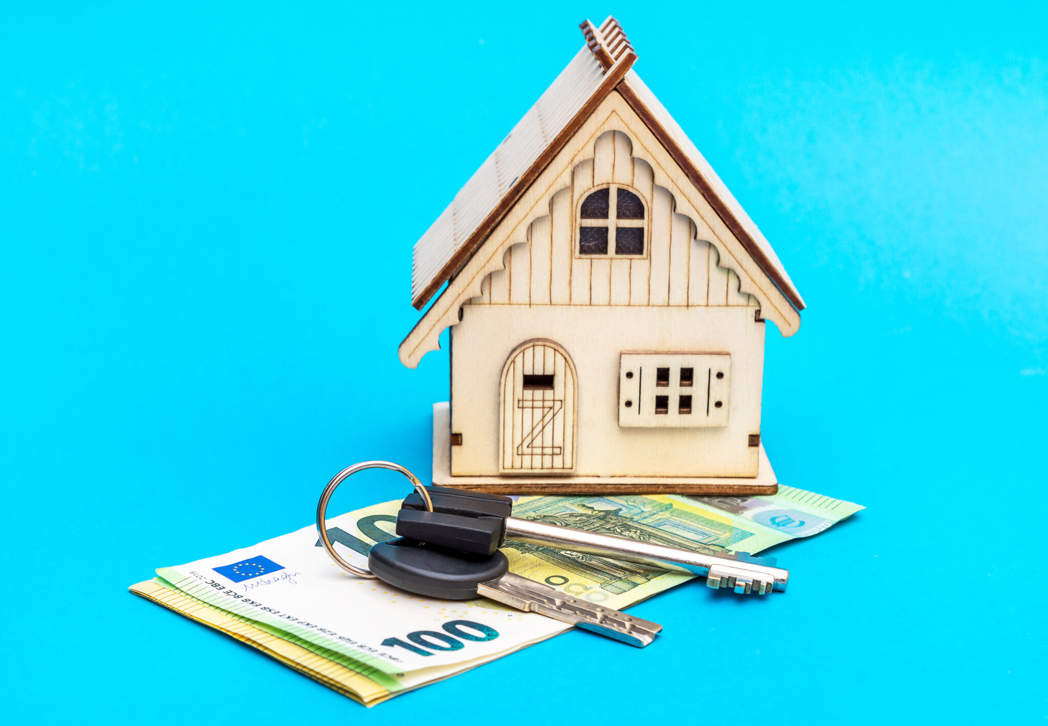 Model of house and keys and euro bills on blue background.